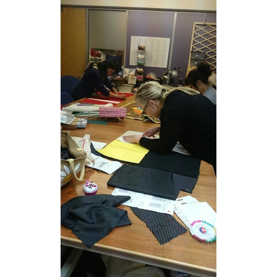 students cutting out on large cutting table in class room. Sewing course madonsewing